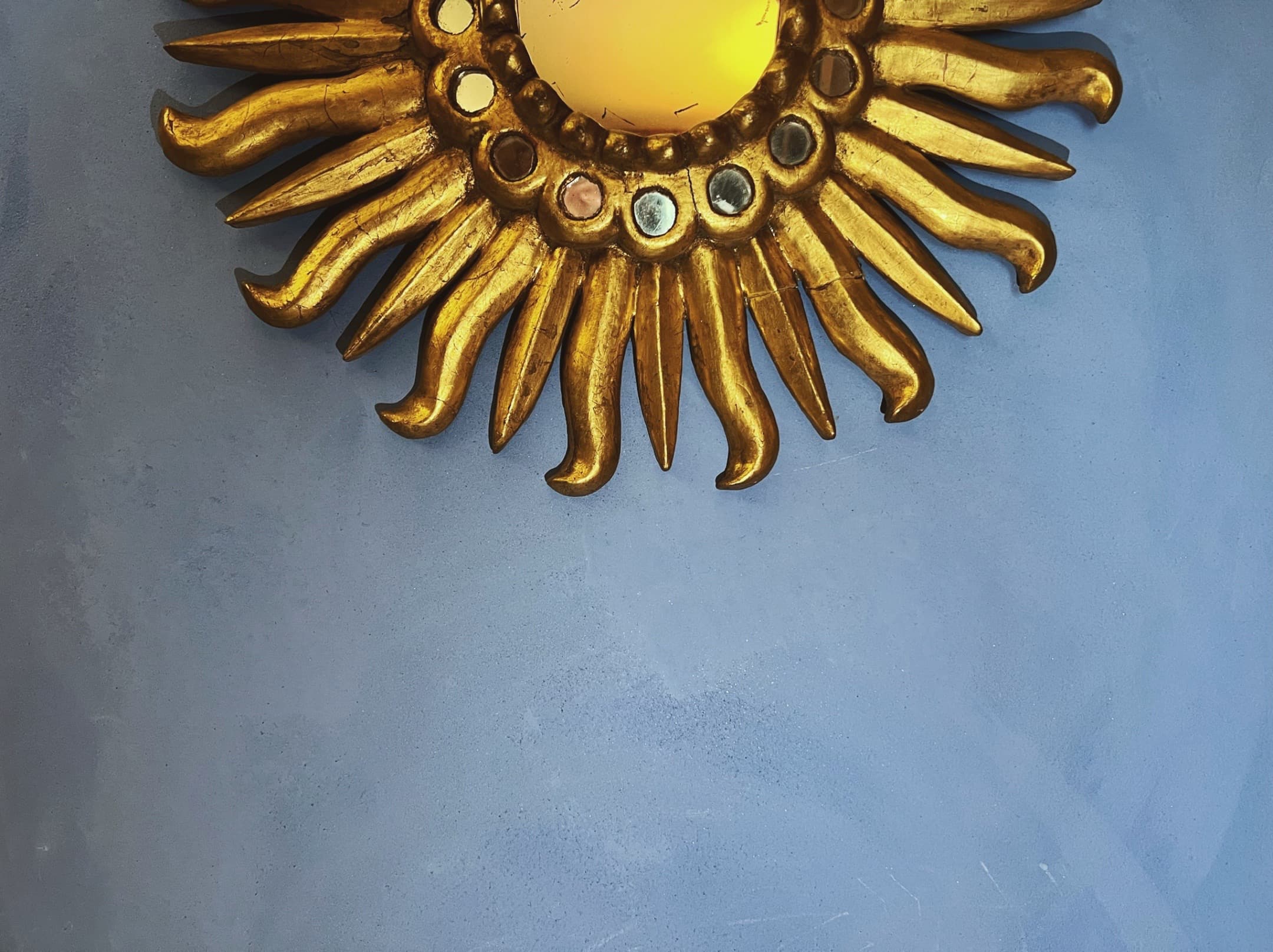 Blue plaster wall with gold sun mirror
